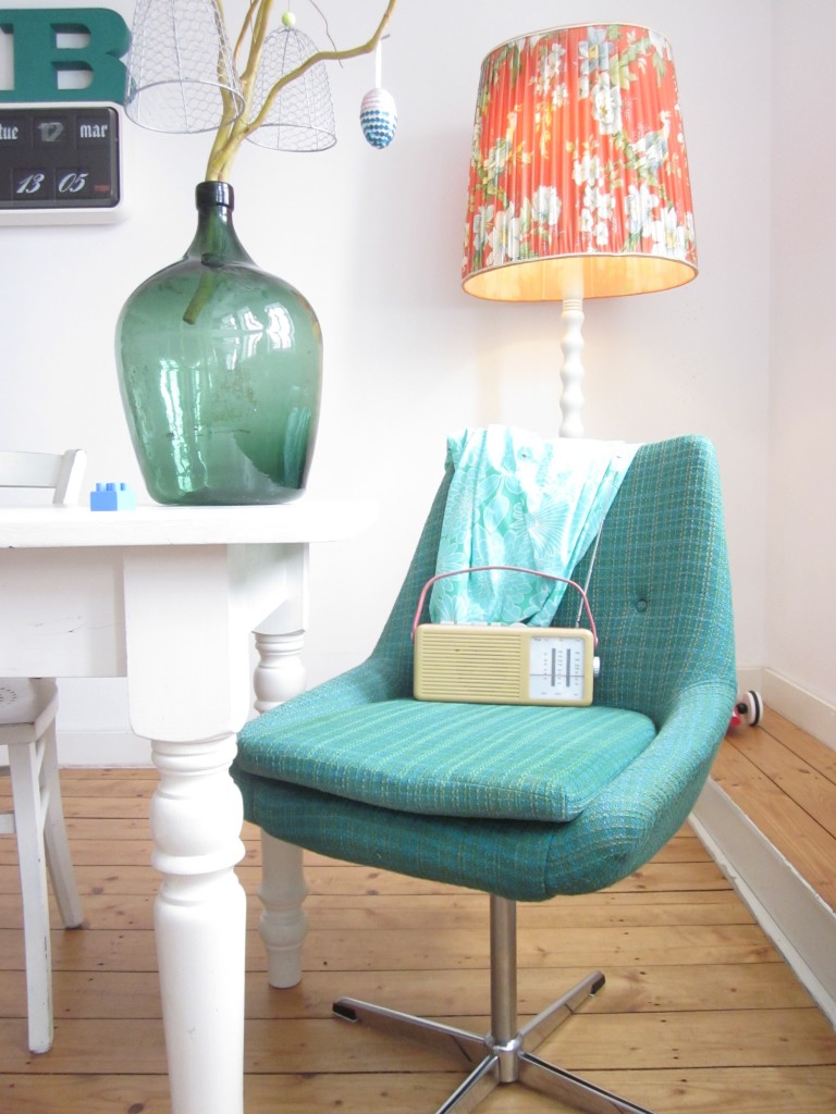 Ein emeraldfarbener Stuhl aus den 60er Jahren steht in meinem Wohnzimmer mit einem Glasballon und einer Flipclockuhr.